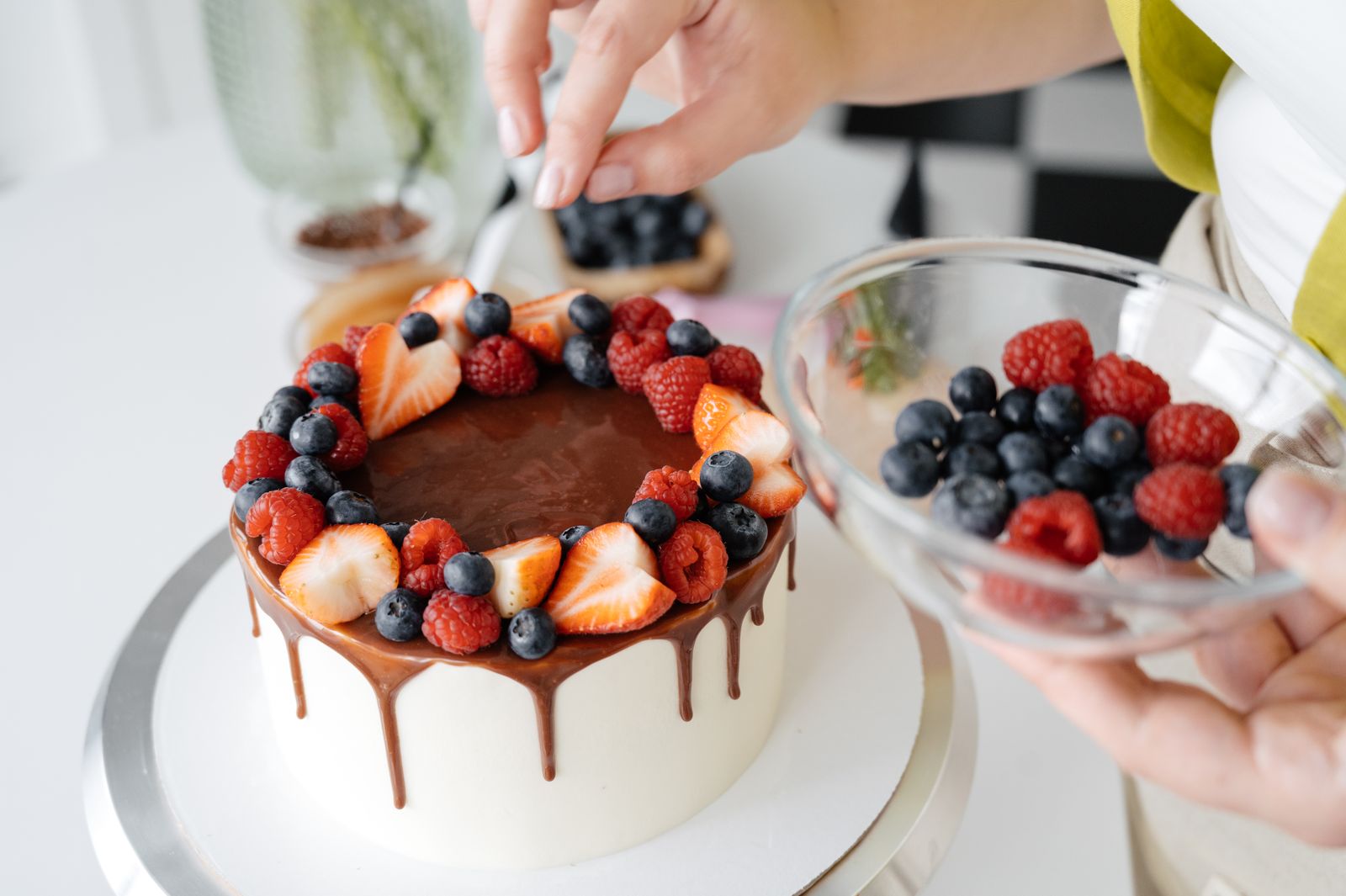 Konditor-Hände dekorieren eine Torte mit Beeren